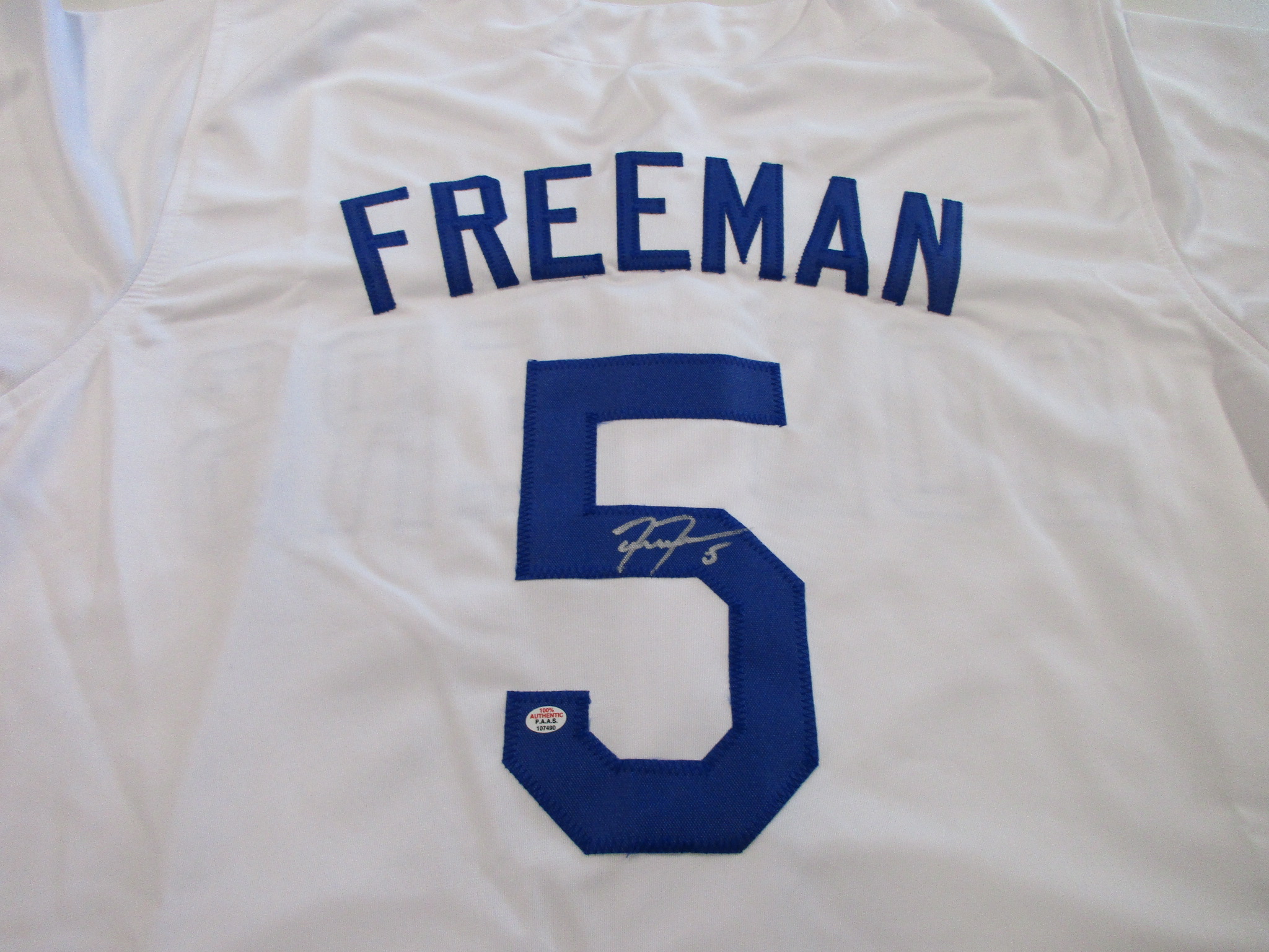 Close-up of white Dodgers jersey back showing 'FREEMAN' nameplate, number 5, and silver ink autograph