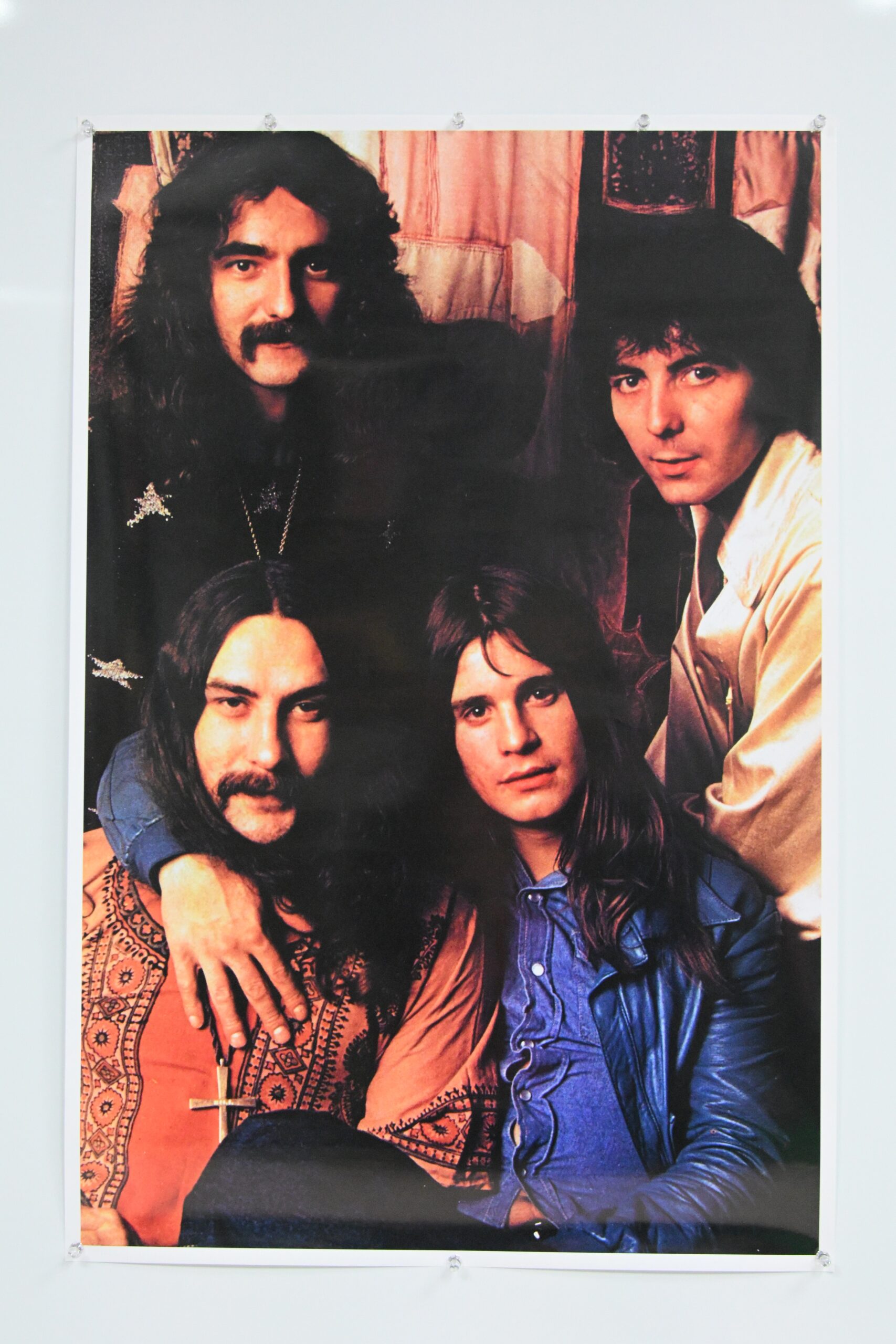 Color photograph of four long-haired men in 1970s rock band style clothing, mounted on a wall with clear acrylic corner clips