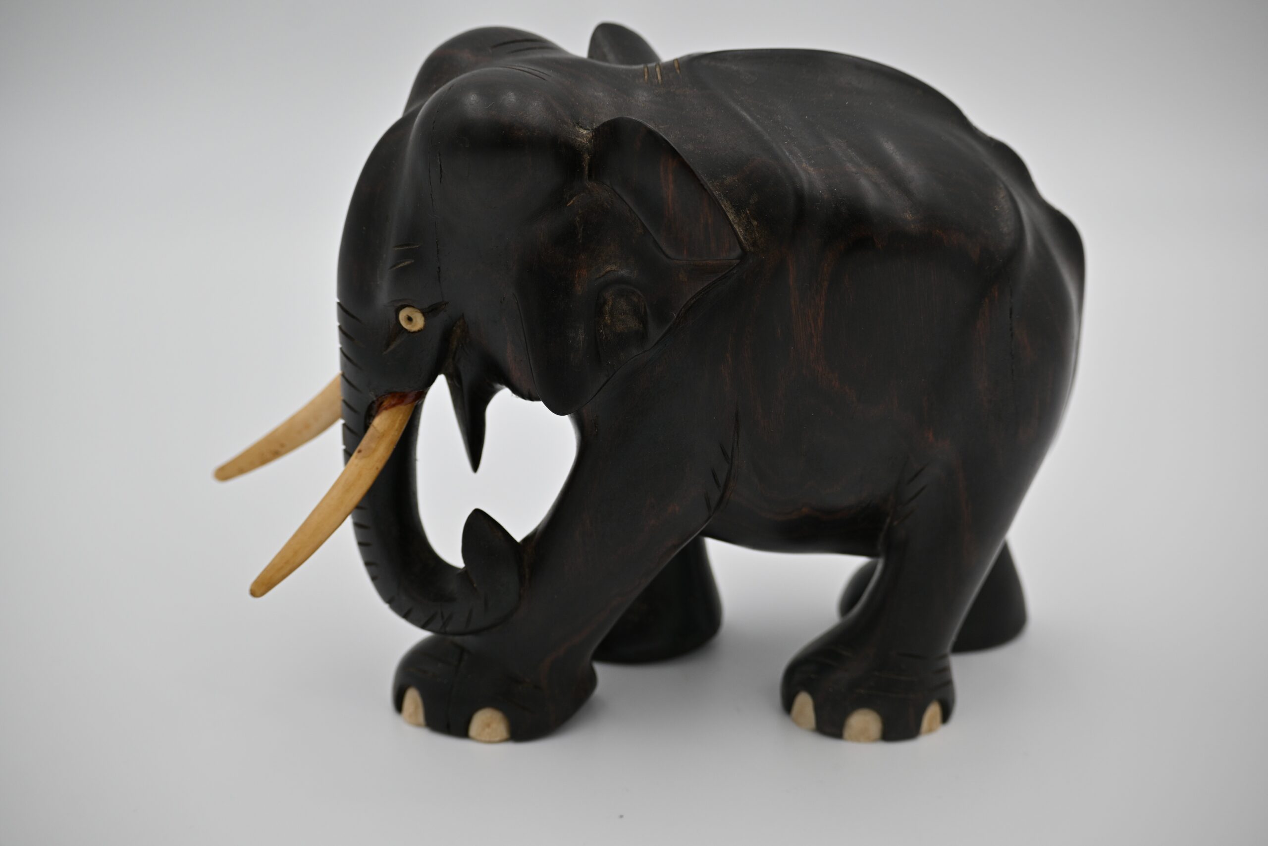 Three-quarter side view of the carved wood elephant with curled trunk and tusks visible