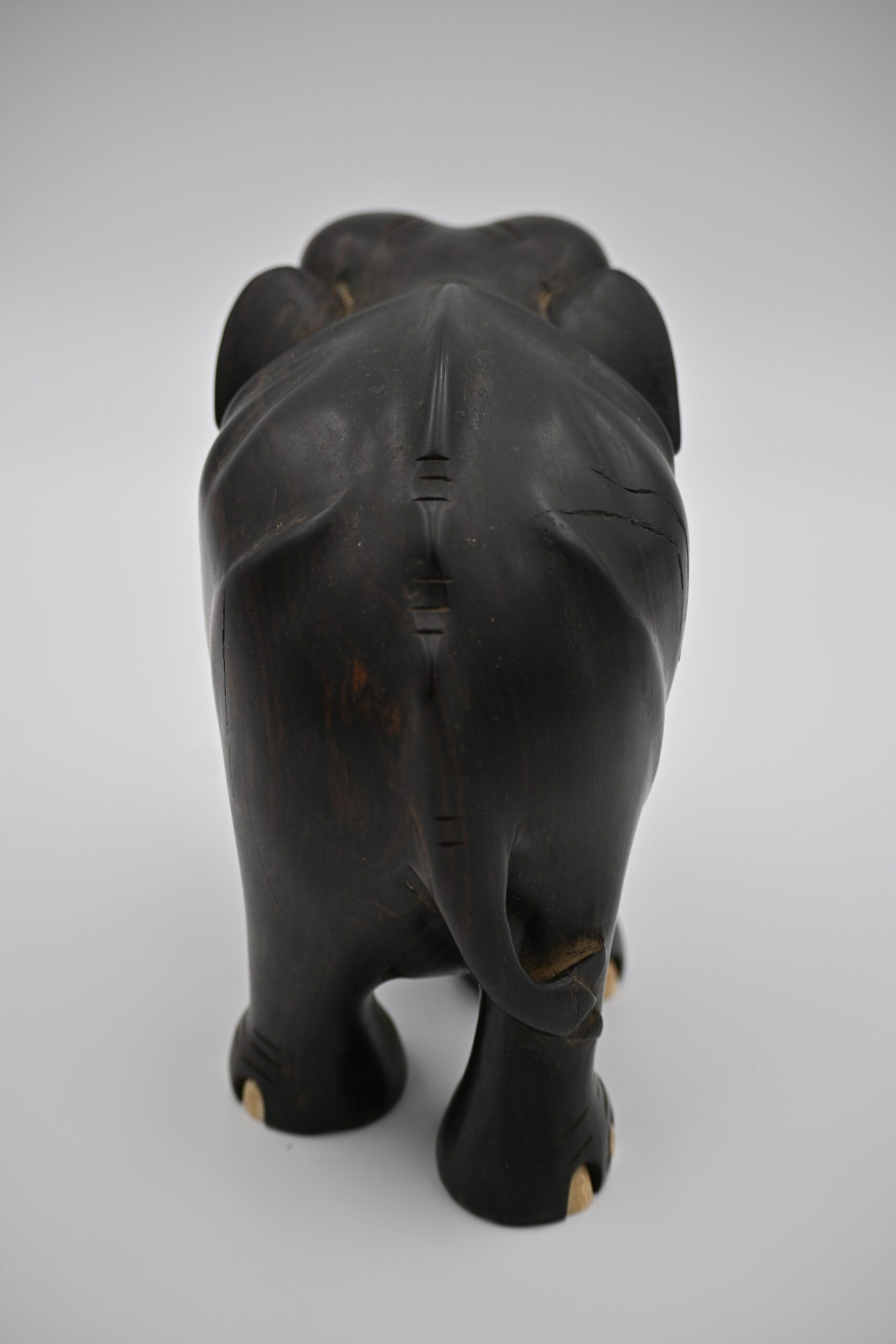 Rear view of the carved wood elephant showing tail, ear detail, and fissure along the back
