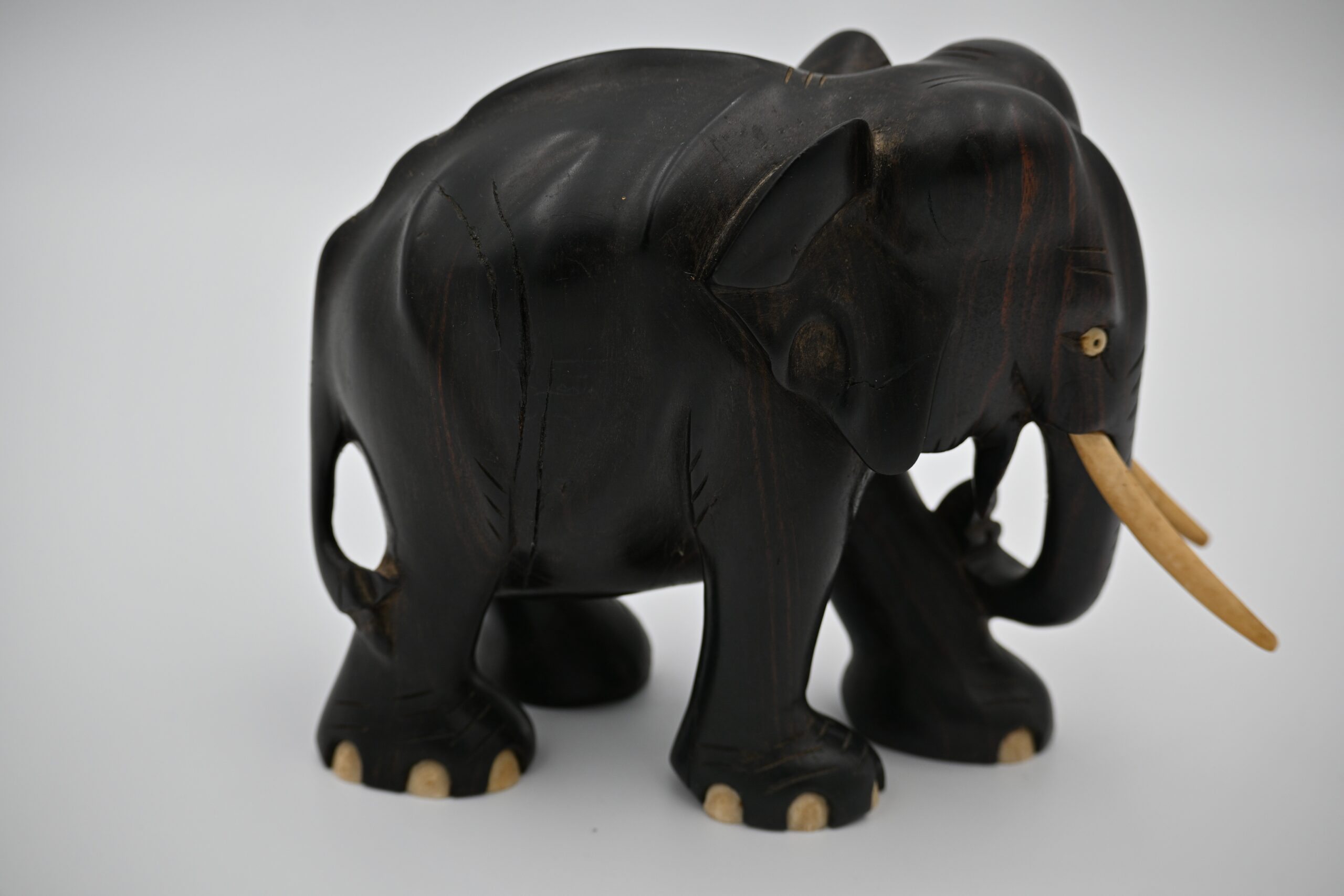 Side profile of the standing carved wood elephant figurine with tusks and textured ear