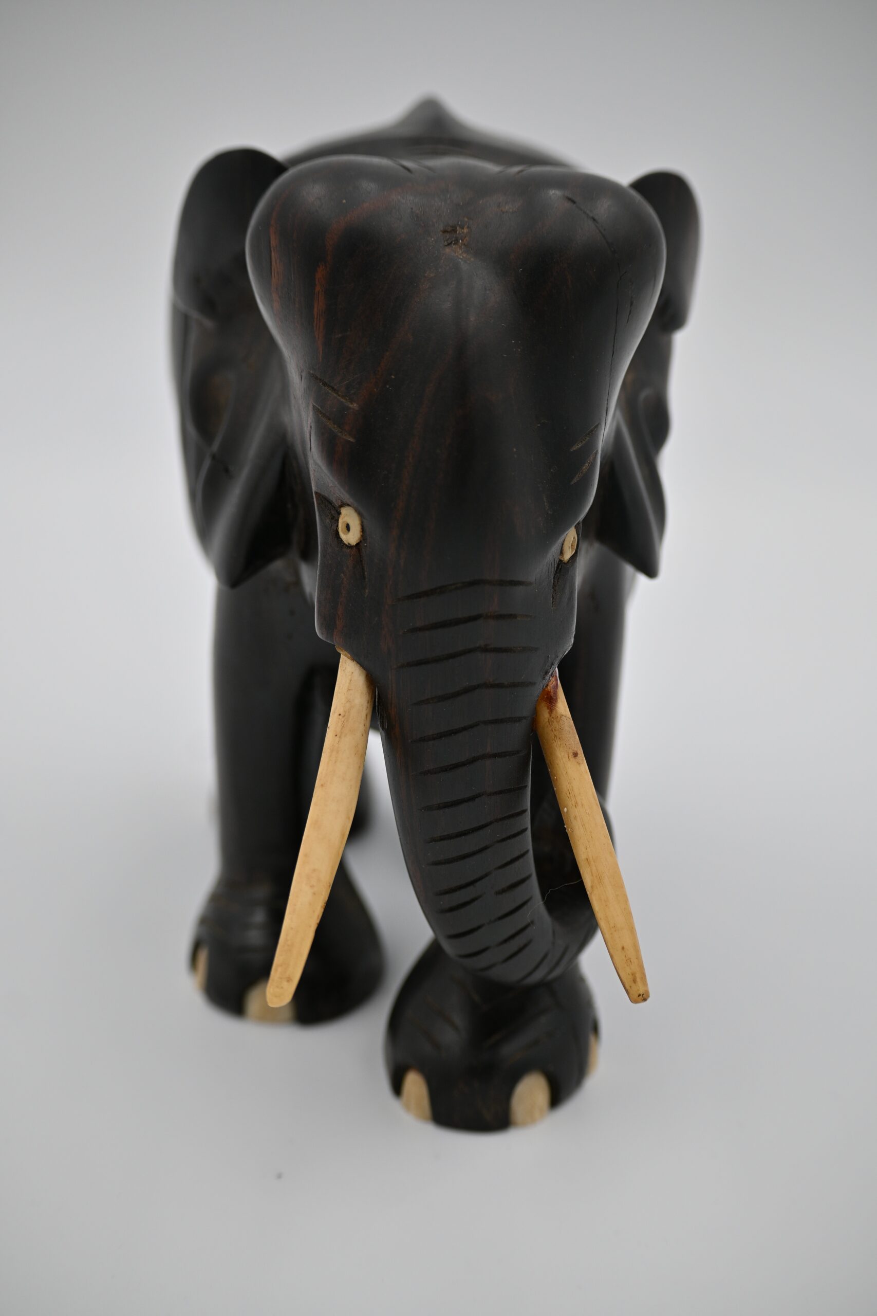 Front view of a carved dark wood elephant figurine showing curled trunk, tusks, and pale inset eyes