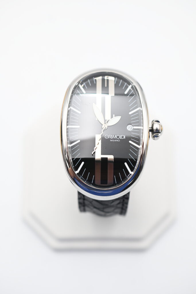 Overhead angled view of the oval Grimoldi Milano watch face and crown against a blurred white background