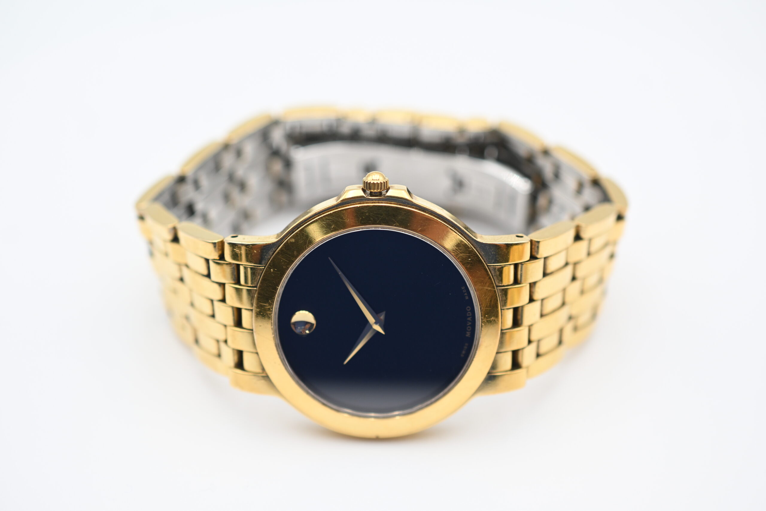 Close-up of the Movado watch face with black dial, gold dot marker, and gold dauphine hands