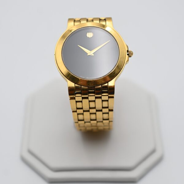 Gold-tone Movado wristwatch displayed upright on a jewelry stand, showing the Museum dot dial