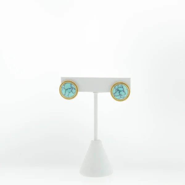 Pair of round turquoise-style clip earrings displayed on a white earring stand