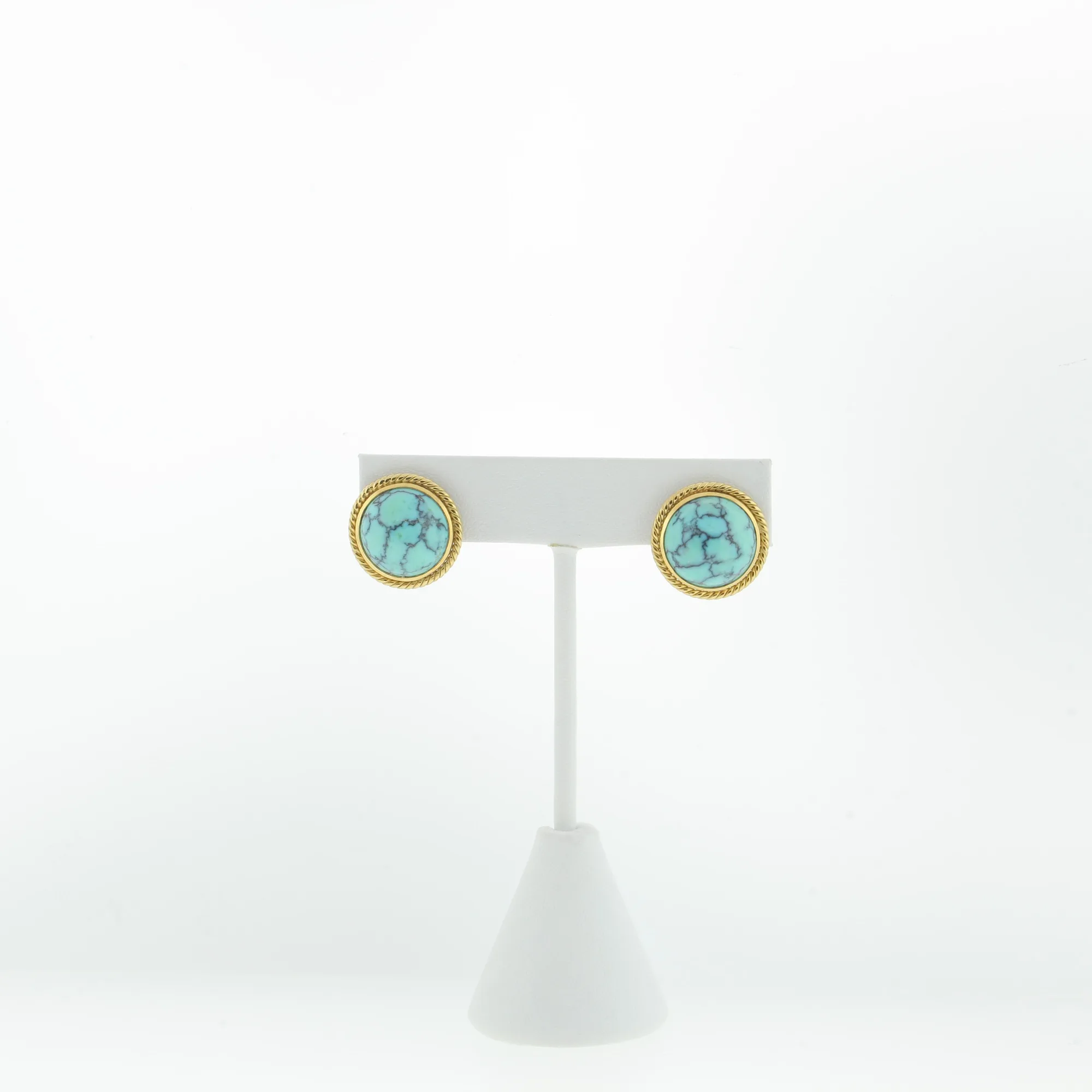 Pair of round turquoise-style clip earrings displayed on a white earring stand