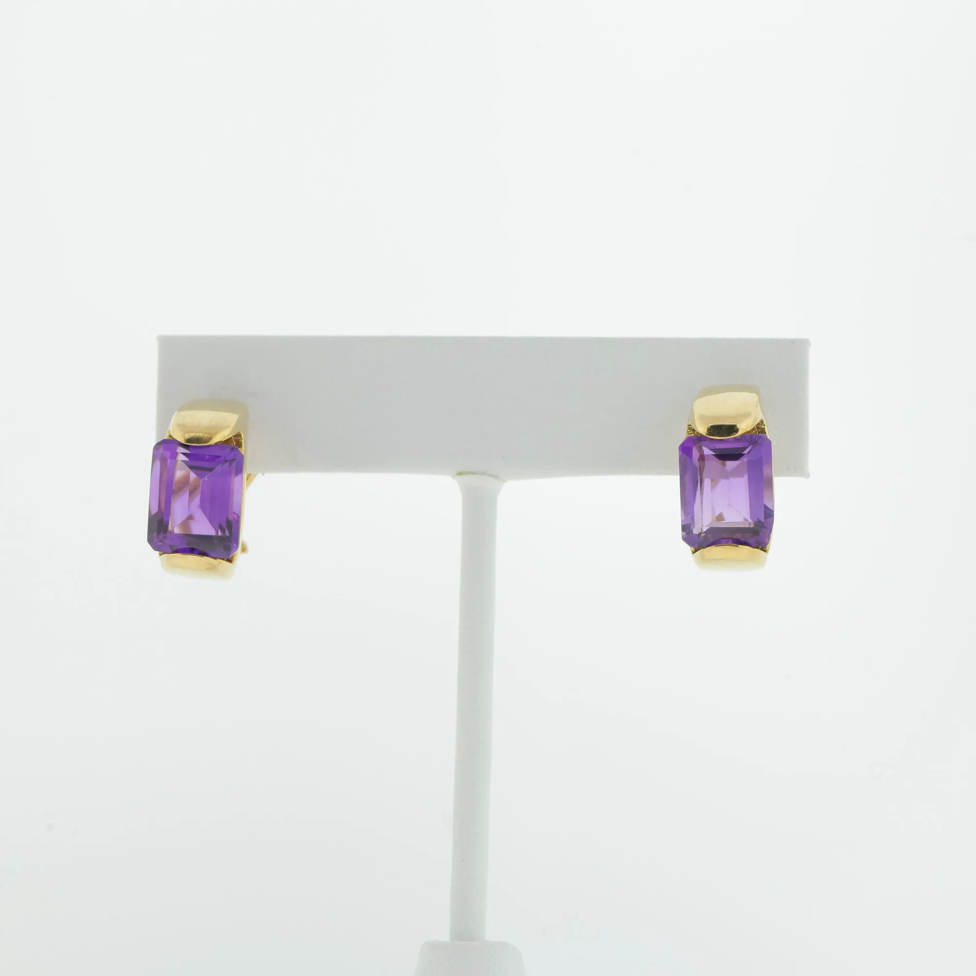 Pair of gold-tone earrings with purple stones displayed upright on a white earring stand
