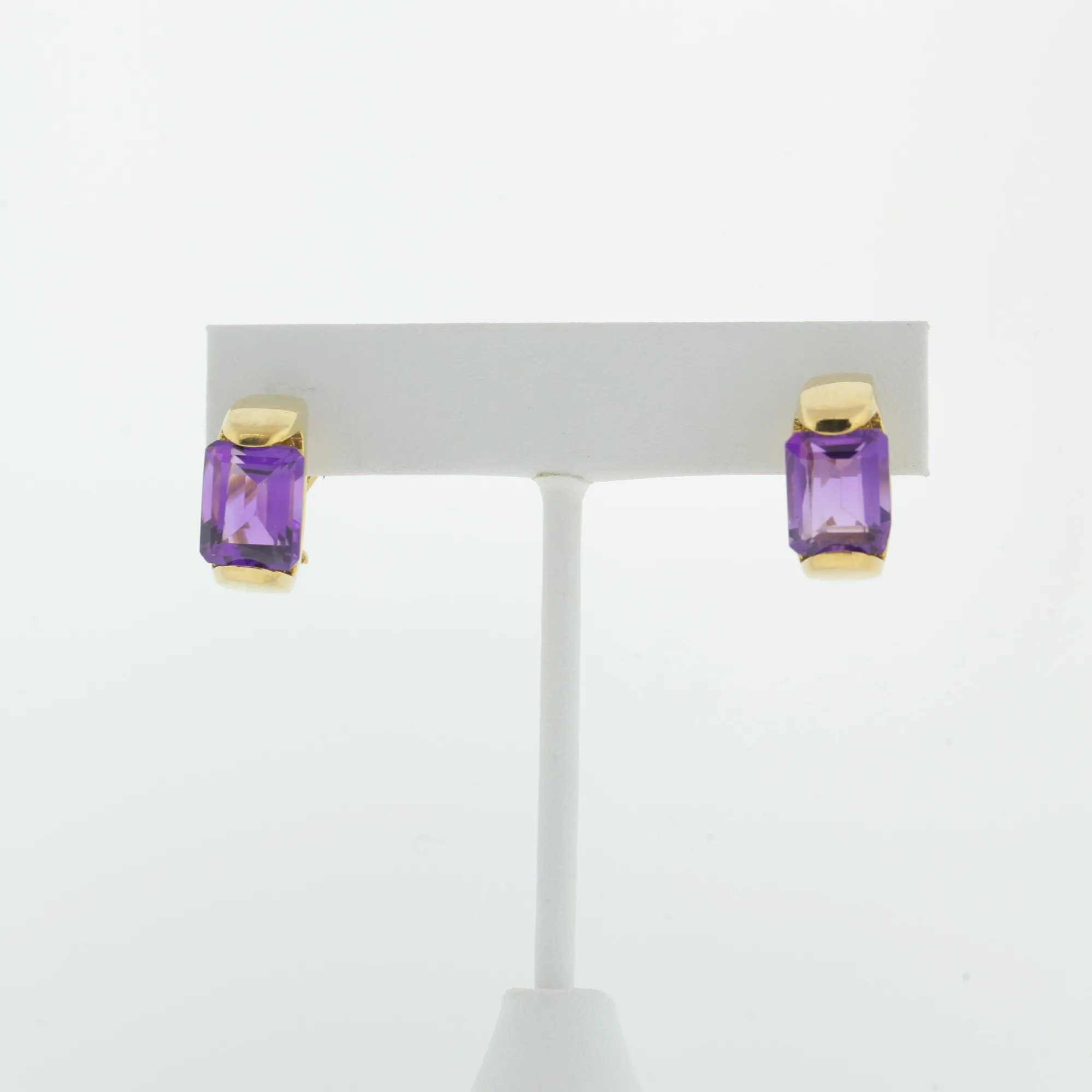 Close view of gold-tone earrings with purple stones on a white T-bar display card