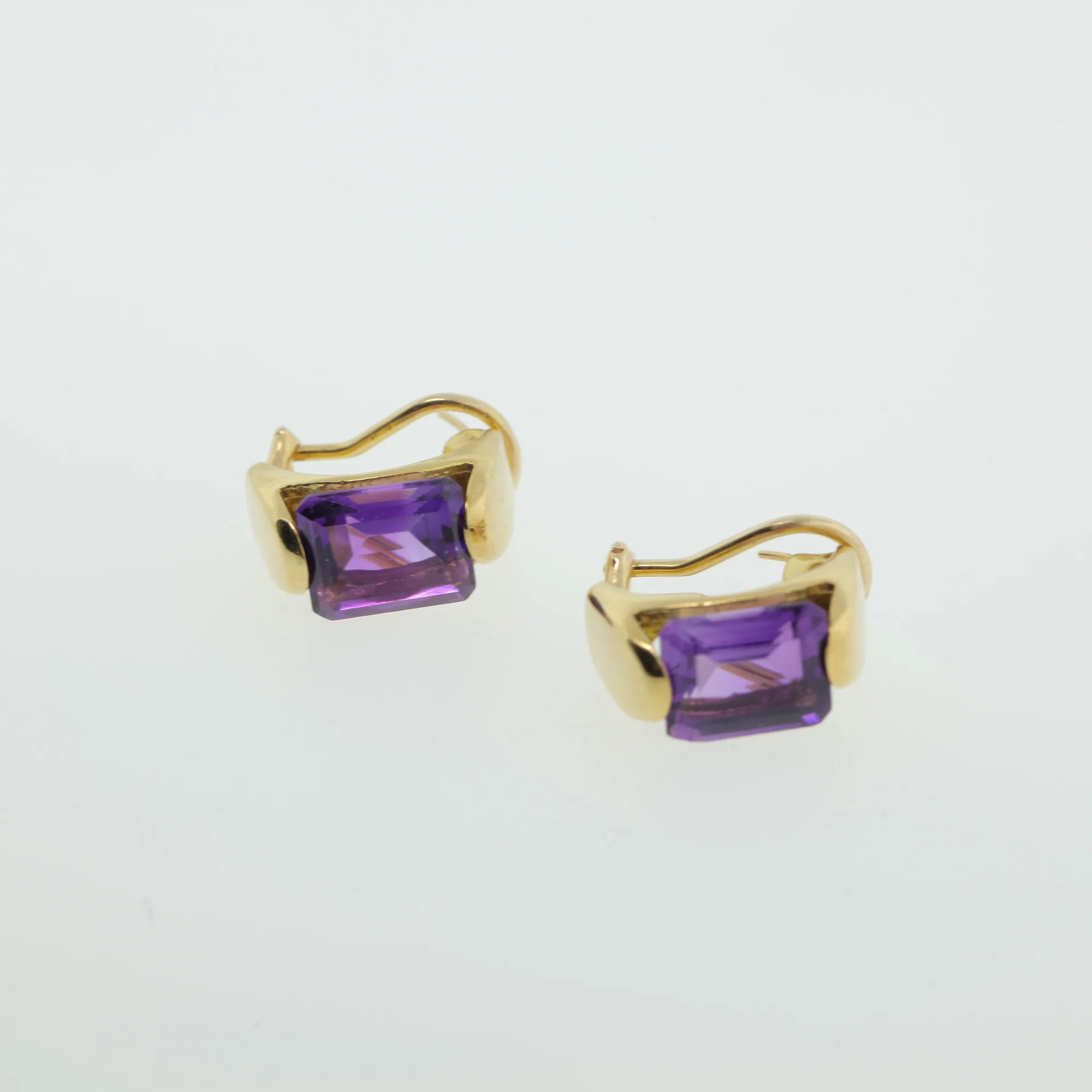 Angled view of gold-tone earrings highlighting the bezel-set purple stones and polished mounts