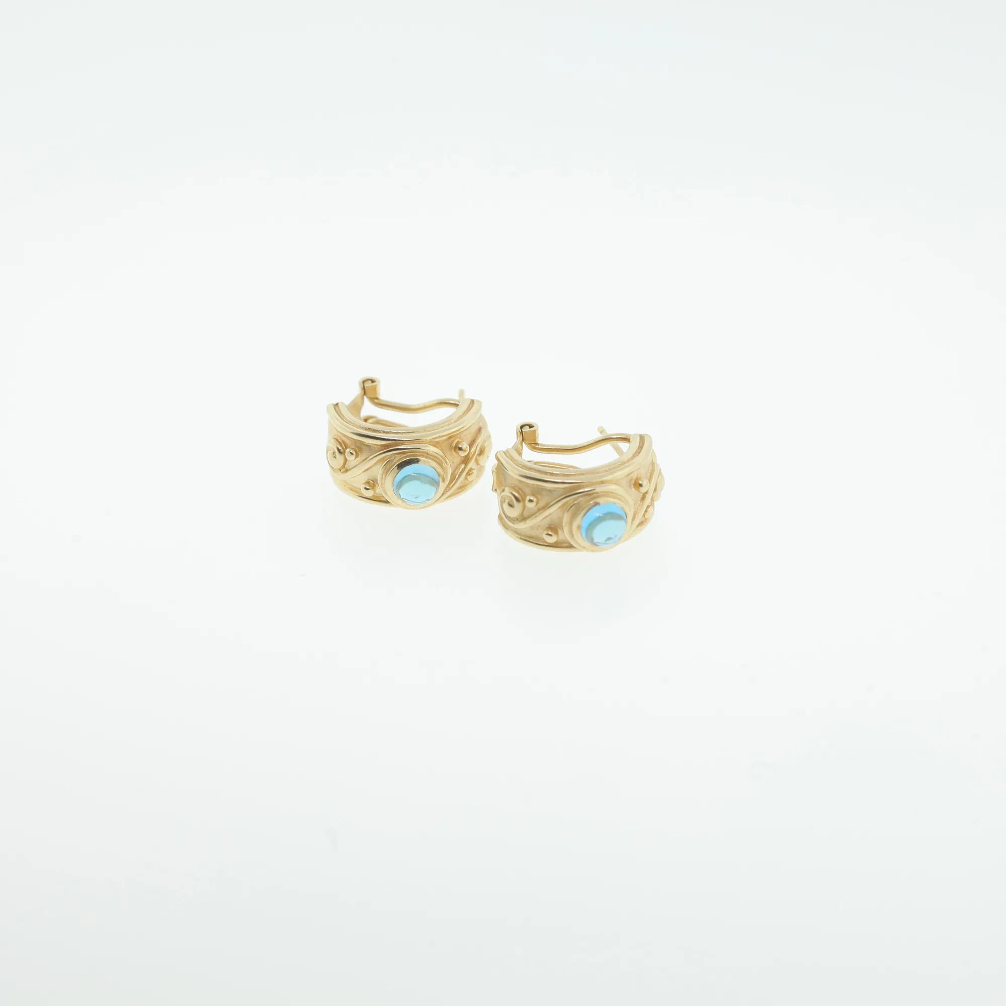 Close-up of gold-tone hoop earrings showing swirl and beaded design with turquoise-blue cabochon centers