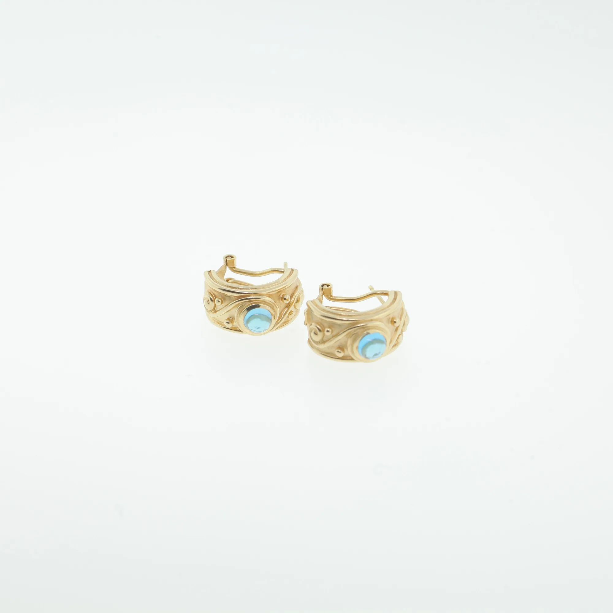 Close-up front view of the scroll and dot patterned hoops with blue cabochon stones