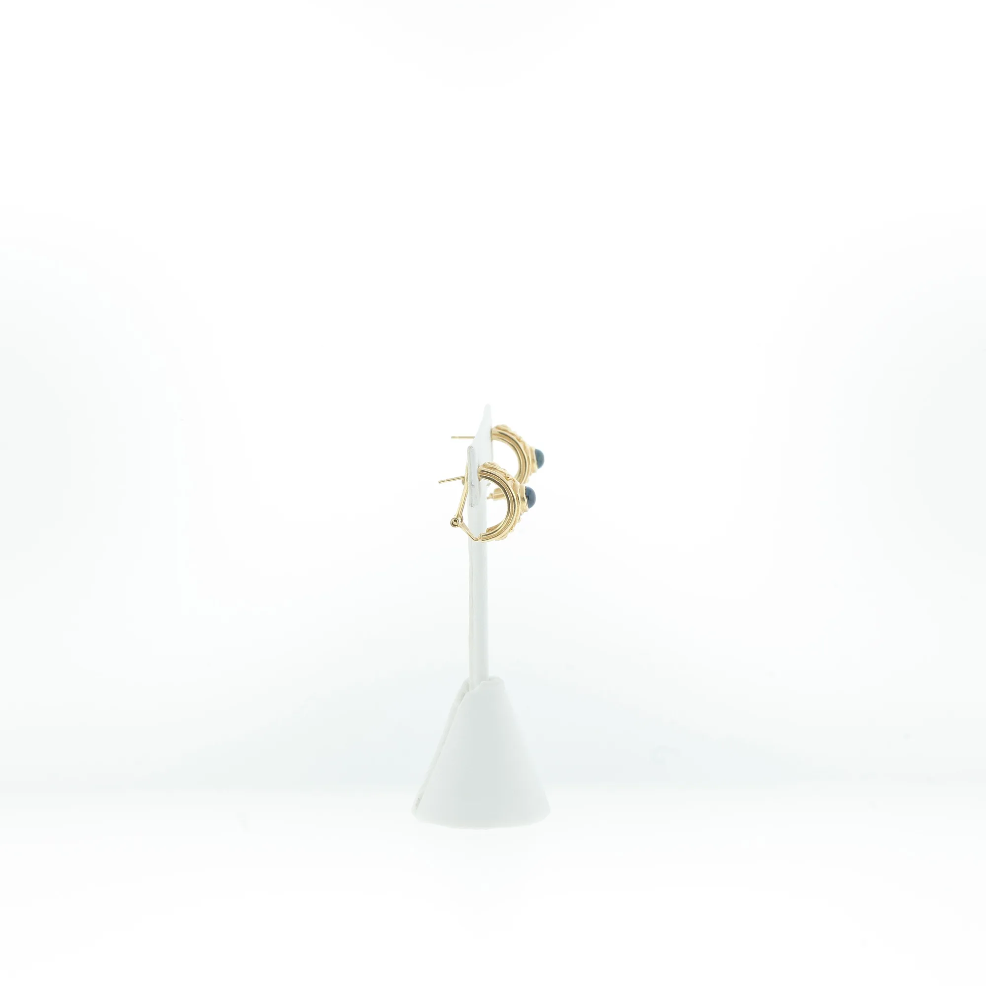 Side view of gold-tone hoop earrings with dark blue cabochon stones displayed on a white earring stand