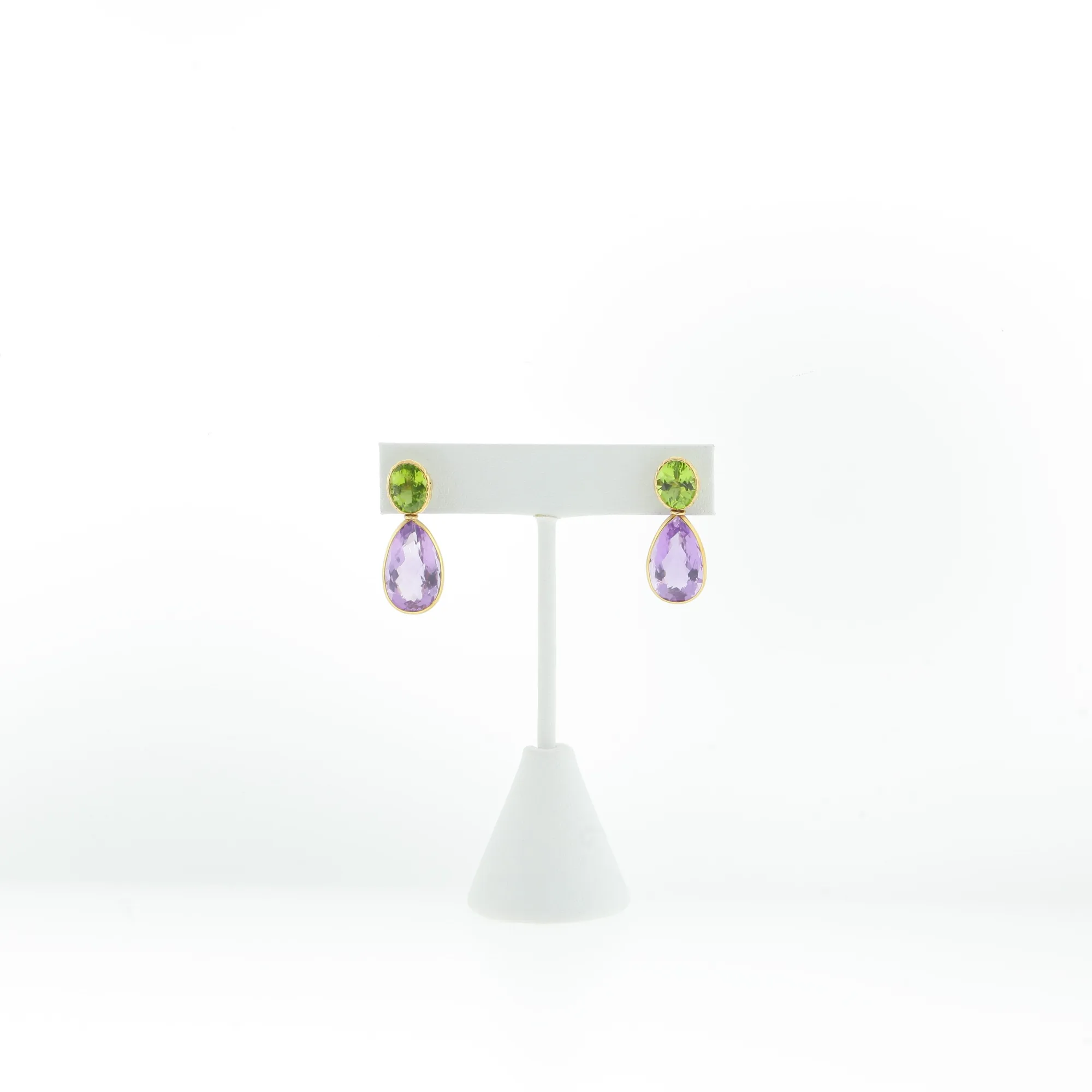 Gold-tone earrings with oval green stones and pear-shaped purple stone drops on a display stand
