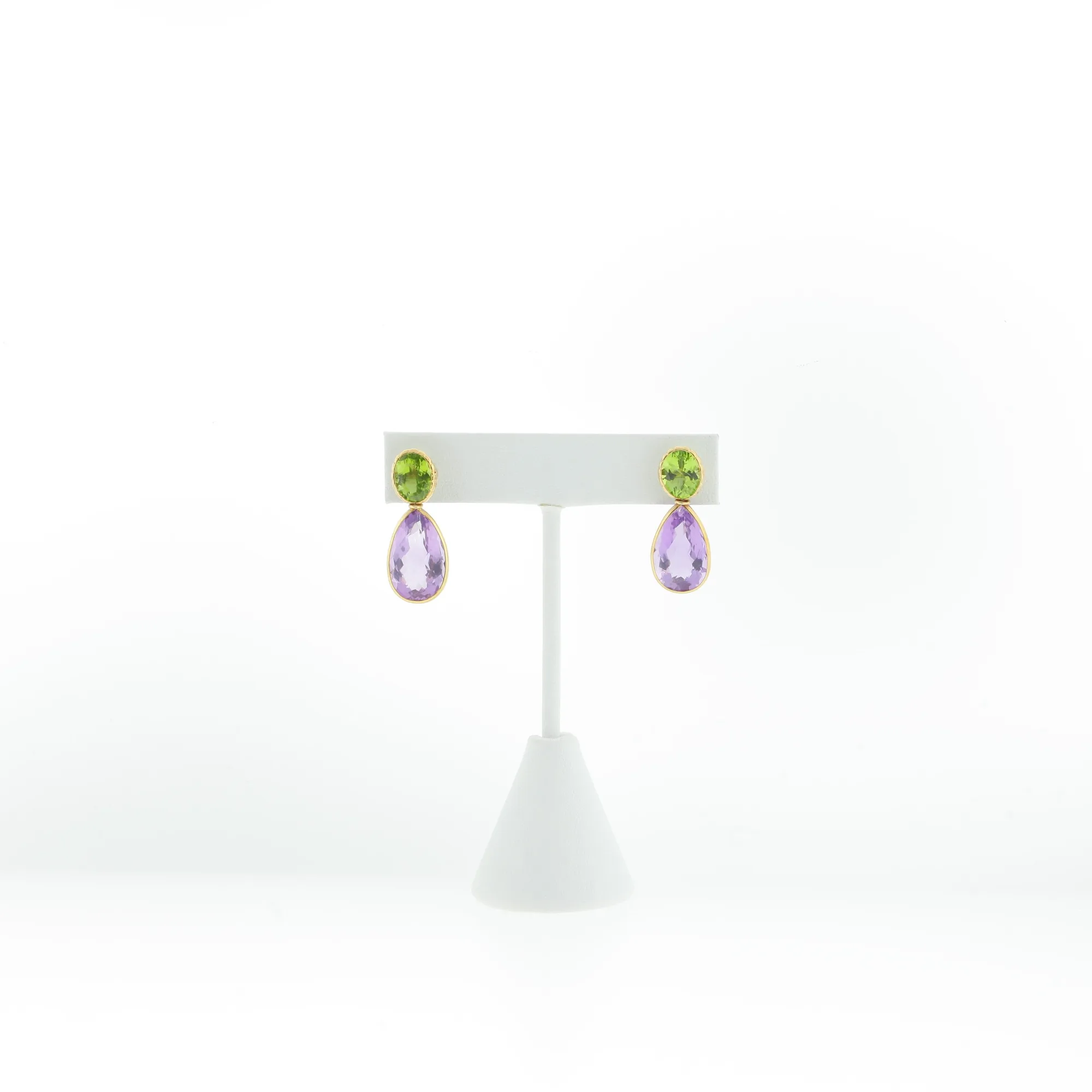 Front view of drop earrings with oval green stones above pear-shaped purple stones on a stand