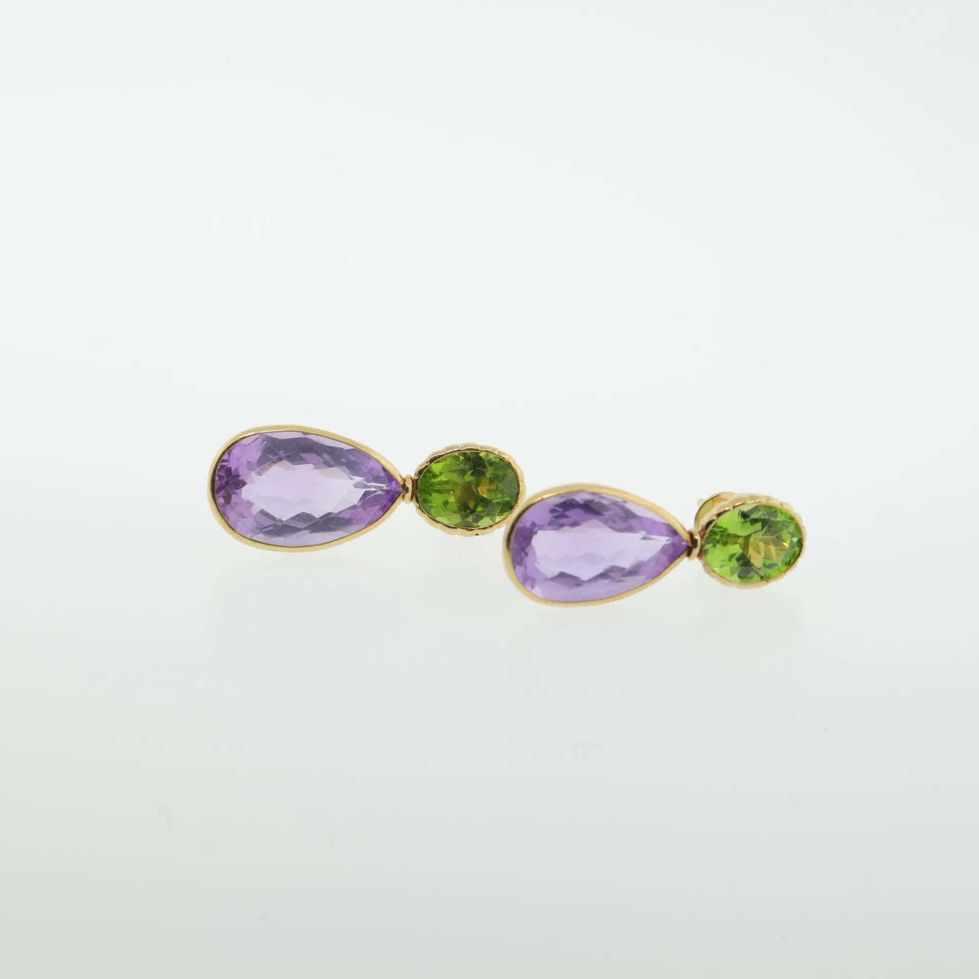 Close-up of gold-tone drop earrings with pear-shaped purple stones and oval green stone accents