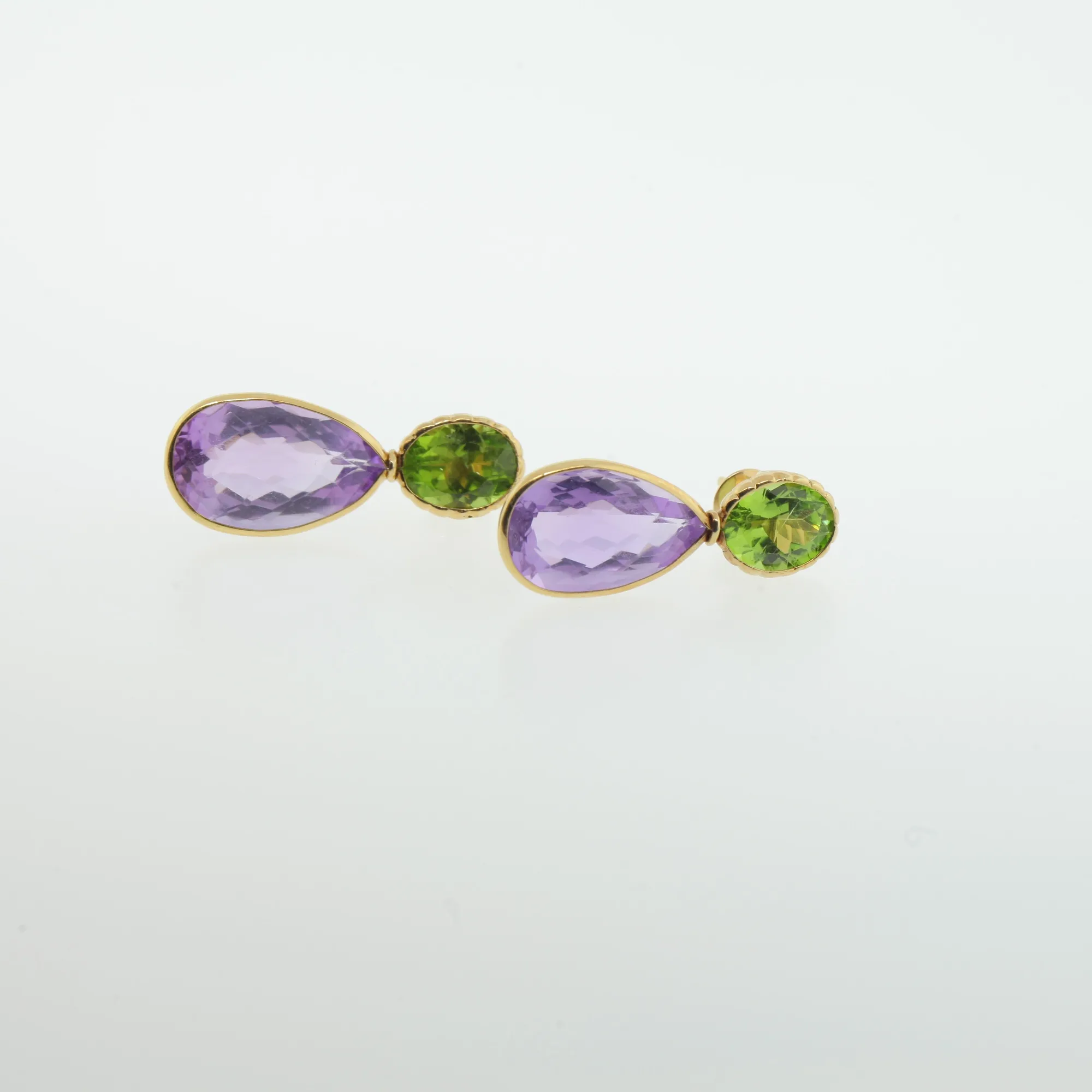 Gold-tone drop earrings with pear-shaped purple stones and oval green stones laid flat on white background