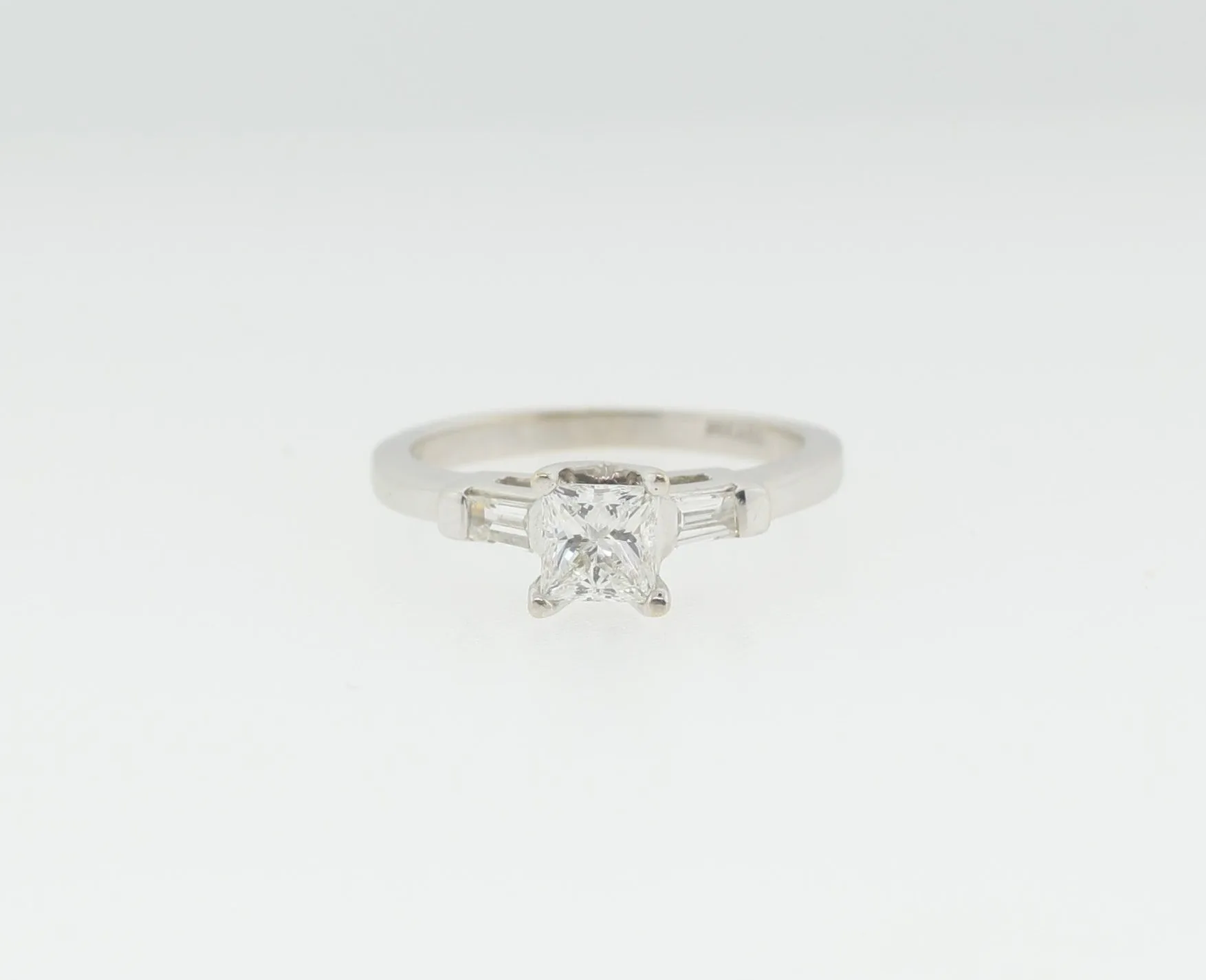 Front view of a white gold ring with a princess-cut center stone flanked by tapered baguette side stones