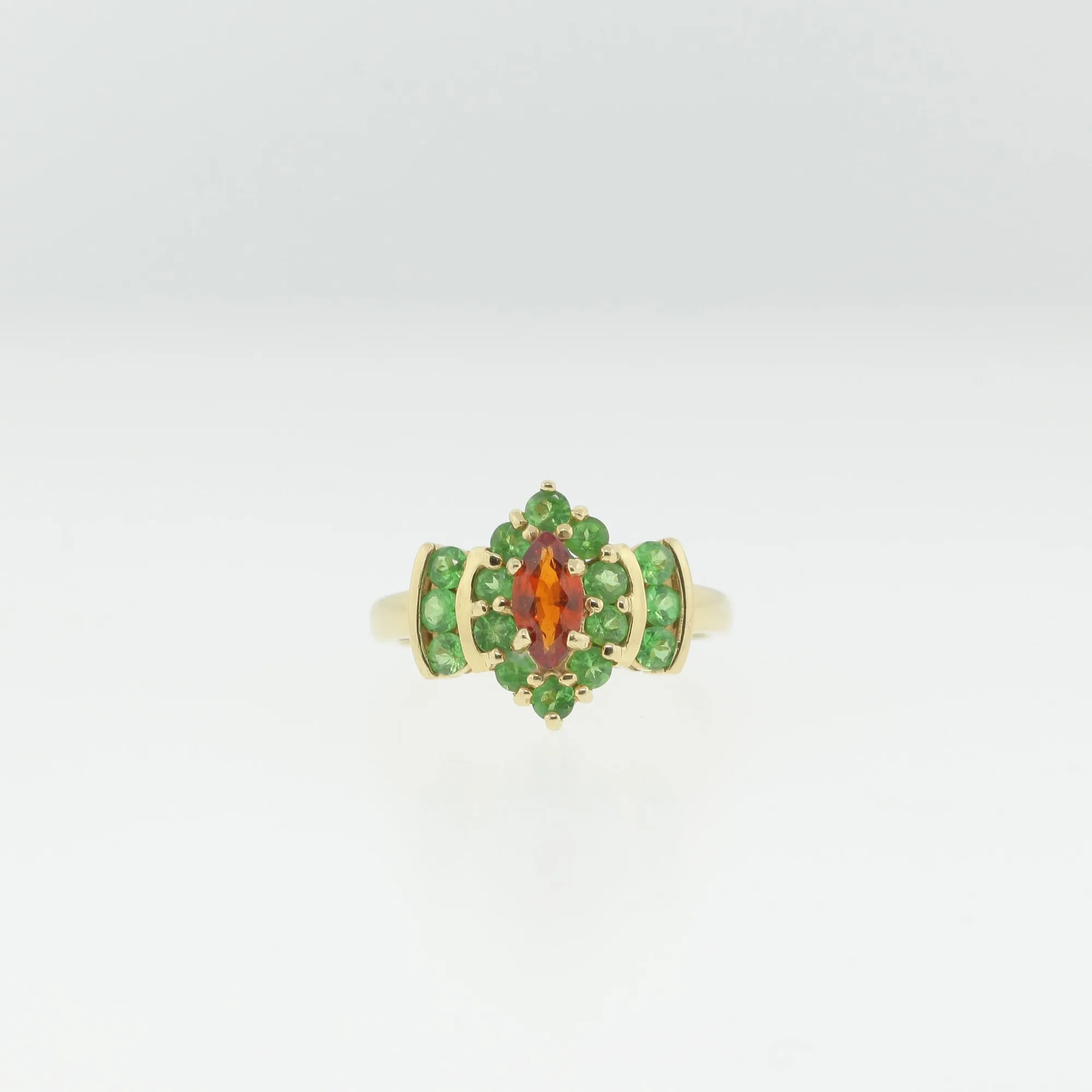 Front view of a 14K gold cocktail ring with an orange-red marquise center stone surrounded by green round stones